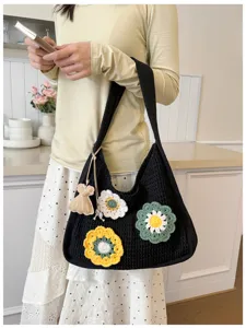 Detailed view of black knitted shoulder bag with colorful crochet flower charms and soft fabric.