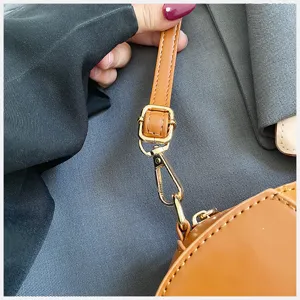 Close-up detail of the brown PU leather handbag strap and shiny golden metal hardware.