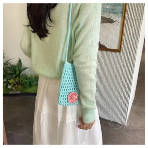 Detailansicht einer hellblauen gehäkelten Handytasche mit rosafarbenem Blumenakzent am Modell.