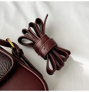 Close-up detail shot of a stylish burgundy leather shoulder bag strap and embossed flap.