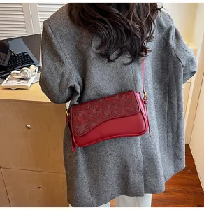 Detail view of wine red embossed shoulder bag worn by model, showing retro floral flap.