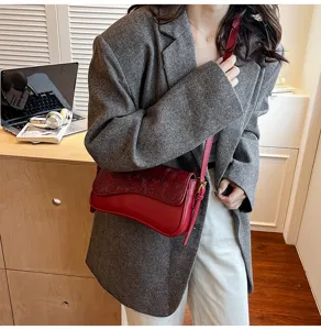 Detailed closeup view of red textured embossed leather crossbody shoulder bag in chic lifestyle scene.