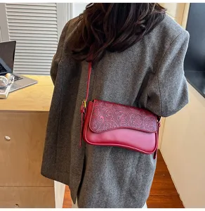 Detailed view of red embossed leather shoulder bag styled with gray blazer outfit.