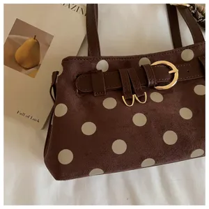 Gros plan détaillé du sac baguette à pois marron, texture suédine et boucle dorée élégante.