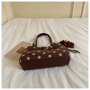 Gros plan du sac baguette en suède marron à pois avec pendentif ours et boucle de ceinture.