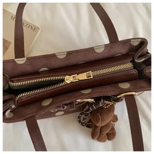 Sac baguette chic à pois marron avec un joli pendentif d'ours en peluche et doubles poignées.