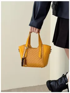 Détail de sac à main en cuir synthétique tissé jaune, avec charm pampille et poignée.