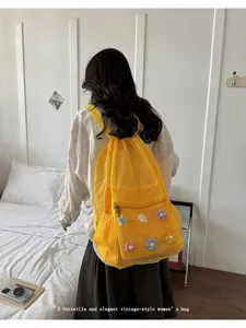 Detailed view of yellow mesh drawstring backpack with cute floral decor in cozy bedroom setup.