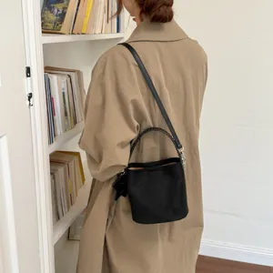 Élégant sac seau noir minimaliste avec poignée tressée et longue bandoulière pour femmes.