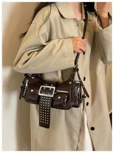 Donkerbruine lakleer schouder motorfiets tas met metalen klinknagels en decoratieve gesp detail.