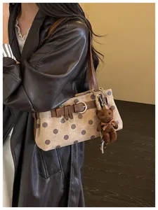 Vue détaillée du sac à épaule baguette marron à pois avec adorable charm d'ours en peluche.