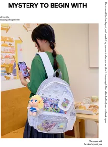 Mochila escolar de lunares grises y blancos con bolsillo frontal transparente y colgante de peluche.