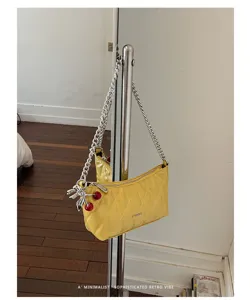 Yellow quilted baguette shoulder bag with silver chain strap and charming cherry pendant detail.