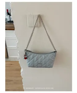 Detailed shot of light blue quilted baguette shoulder bag with metal chain and cherry charm.