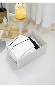 Caja de almacenamiento de tela blanca para el hogar, vista detallada de ropa doblada.