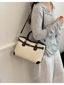 Chic cream canvas shoulder bag with dark brown leather trim, top handles, and buckle strap detail.