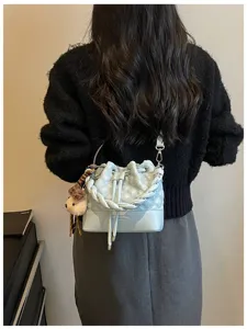 Detailed view of the light blue quilted bucket bag with braided handle and cute bear pendant.