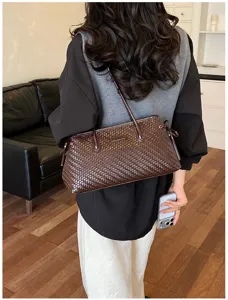 Vista detallada de un elegante bolso de hombro de cuero tejido marrón en un interior moderno.