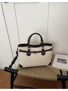 Canvas tote bag detail showing dual top handles, contrast leather trim, and chic metal buckle.