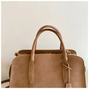 Brown suede Boston bag detail, top handle and metallic hardware close up product view.