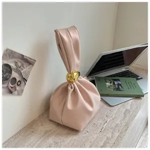 Detailansicht der eleganten rosa Plisseetasche mit glänzendem goldenen Ringgriff.