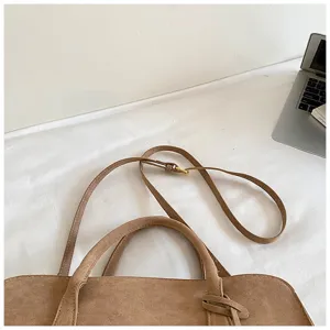 Brown suede handbag detail closeup showing top handles and adjustable shoulder strap feature