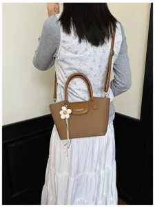 Detail view of the brown leather dumpling handbag featuring a cute floral charm and strap.