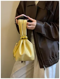 Detailaufnahme einer trendigen gelben Falten-Handgelenk-Eimertasche mit goldenem Ring.