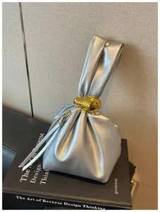 Nahaufnahme der silbernen metallischen Plissee-Handtasche mit goldenem Ringdetail.