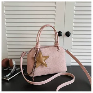 Nahaufnahme einer stilvollen rosa Handtasche mit Sternanhänger auf dunklem Tisch.