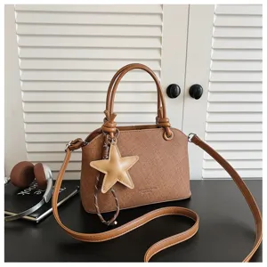 Detailaufnahme der braunen Ledertasche mit Sternanhänger auf schwarzem Tisch mit Lamellentür.
