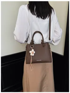 Vista detallada del elegante bolso marrón de hombro con cuero texturizado y colgante floral.