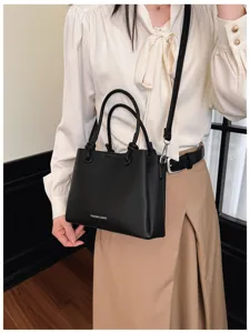 Detalle de elegante bolso negro texturizado, con asas dobles y correa para el hombro.