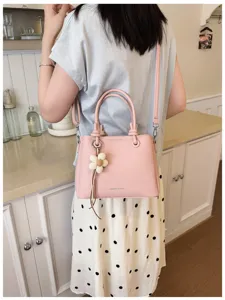 Bolso cubo cruzado elegante rosa con dijes florales, diseño texturizado minimalista.