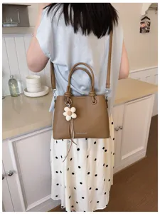 Vista detallada de un elegante bolso tipo cubo marrón con colgante de flor y correa cómoda.