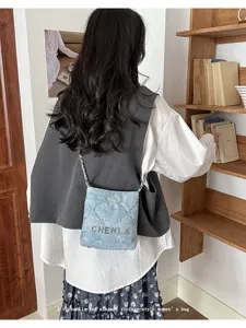 Denim crossbody bag detail showcasing rhinestone studs and chic chain strap in room view.
