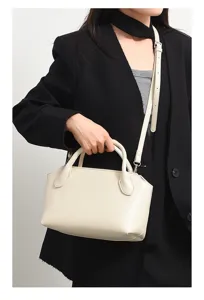 Close-up detail of cream bowling bag with top handles and shoulder strap worn by model.