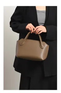 Close-up of a stylish brown leather handbag held by hand, showing daily retro style.