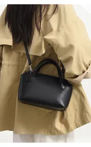 Detailed view of black leather bowling bag with top handles and shoulder strap worn.
