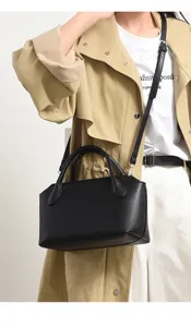 Detail shot of black leather bowling bag with top handle and shoulder strap worn by model.