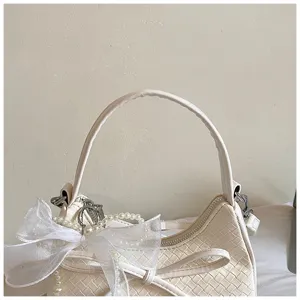 Detail view of white woven shoulder bag featuring an elegant organza bow and pearl charm.