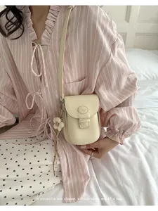 Detailed view of vintage beige cross-body mini bag with floral charm and slim strap.