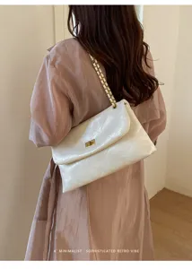 Detailed view of the white quilted shoulder bag with chain strap and gold turn lock.