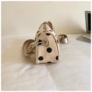 Gedetailleerd zijaanzicht van beige schoudertas met zwarte stippen en brede riem.