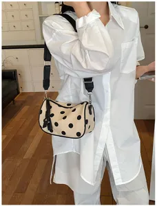 Detailopname van een chique beige schoudertas met zwarte stippen en een zwarte band.