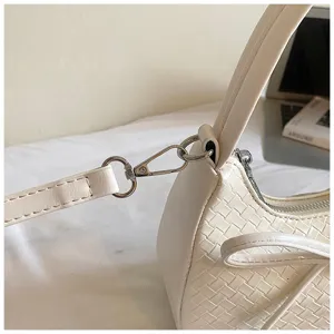 Close-up detail of white woven leather crescent shoulder bag featuring metal hardware and strap.