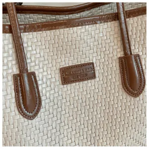Détail du sac cabas tressé beige avec poignées en cuir marron et écusson de logo élégant.