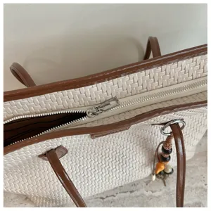 Gros plan sur la fermeture éclair et le charm du sac tressé, montrant texture et quincaillerie.