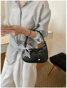 Black woven leather crescent underarm bag with pearl bow charm, stylish fashion style.