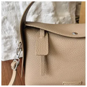 Detail view of beige leather shoulder bag, premium texture, metal hardware and elegant strap.